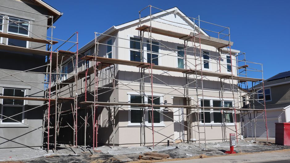 View of a modern two-story house under construction with scaffolding on a sunny day.